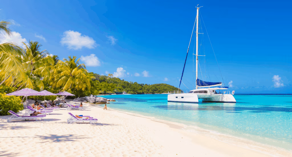 Purple-striped umbrellas and beach chairs on a sand cay in Fiji, with the Sabre sailing catamaran anchored in the turquoise water nearby