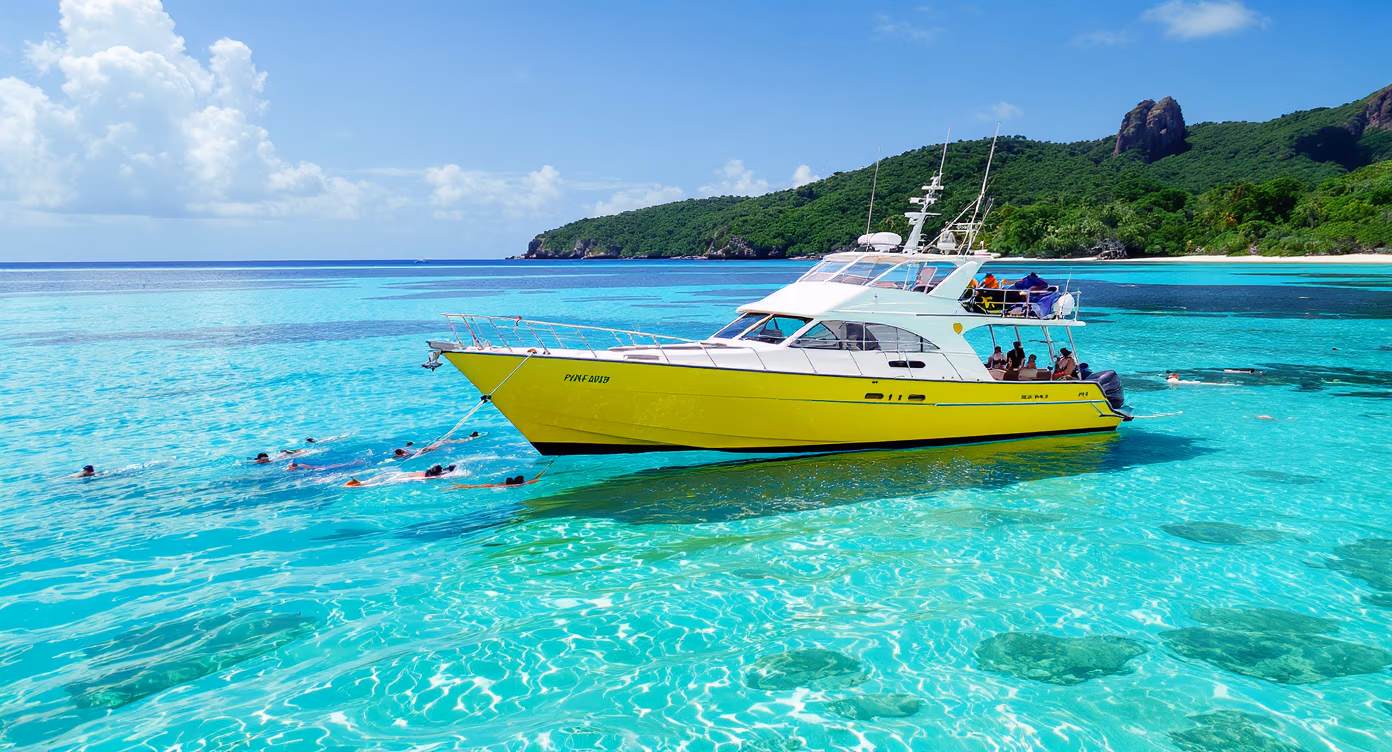 Guests in snorkel gear enjoying the shallow waters near a yellow Cruisin Fiji boat anchored by an island in the Mamanucas
