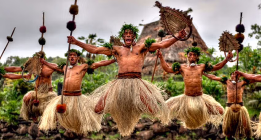 Traditional Fijian Culture Village with thatched huts, kava ceremony, cultural dancing, and local artisans demonstrating crafts surrounded by tropical greenery.