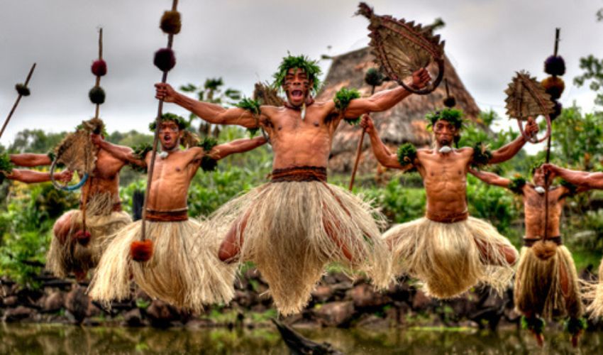 Traditional Fijian Culture Village with thatched huts, kava ceremony, cultural dancing, and local artisans demonstrating crafts surrounded by tropical greenery.